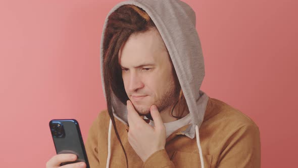 Young Thoughtful Man Browsing Mobile Phone on Pink Background