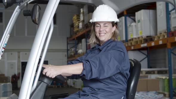 Smiling Female Employee Sitting in Forklift in Warehouse