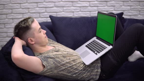 Young Student Man Relaxing on Sofa Looking Laptop Green Screen Mockup