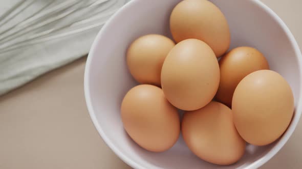 Video of overhead view of white bowl with eggs and egg whisk on beige background