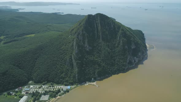 Aerial View of the Tall Mountain Covered By the Forest Towering Over the Empty Valley and Sea on