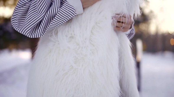 Young Beautiful Girl Spends Her Hand with Red Nails on a White Fur Vest