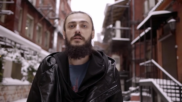 Young Bearded Man in the Costume of the Assassin Is on an Abandoned Snowy City Day