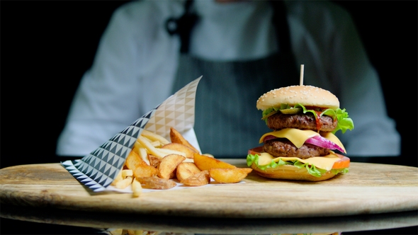 Chef Is Serving Set of Tasty Burger, French Fries, Beer on the Wooden Tray on the Black Background