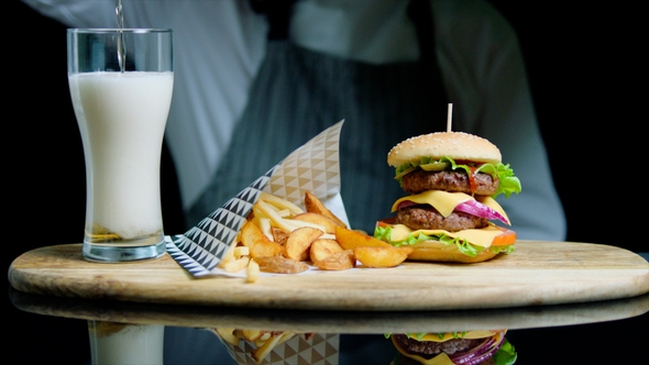 Chef Serving Set of Tasty Burger, French Fries, Pouring Beer Into Glass on Wooden Tray