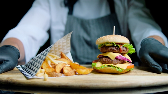Chef Is Serving Set of Tasty Burger, French Fries, Beer on the Wooden Tray on the Black Background