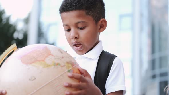 African American Schoolboy in School Clothes with a Backpack Playing with a Globe