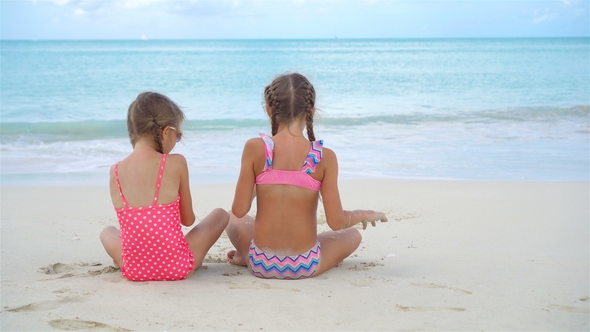 Two Little Happy Girls Have a Lot of Fun at Tropical Beach Playing Together with Sand