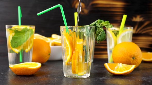 Pouring Water in a Glass with Fresh Cutted Slices of Oranges