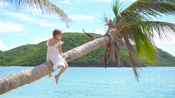 Adorable Little Girl at Tropical Beach Sitting on Palm Tree During Summer Vacation