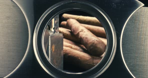 Cigars in humidor with lighter view through a cigar cutter.