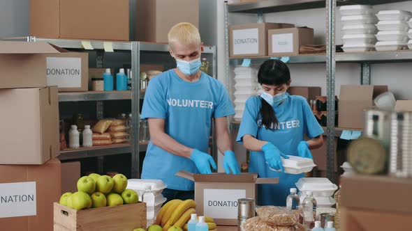 Man and Woman in Face Masks Packing Donation Boxes