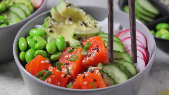 Poke bowl with salmon, rice, avocado, edamame beans, cucumber and radish in gray bowl