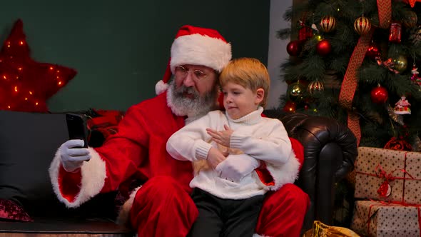 Santa Claus with a Child Sitting on His Lap Are Taking a Selfie Using a Smartphone