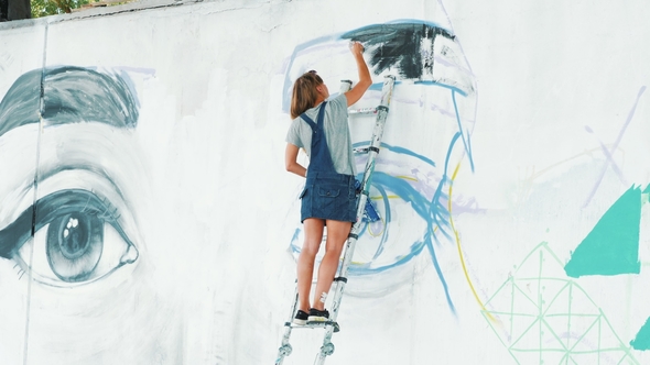 Beautiful Young Blonde Girl Making Graffiti of Big Eye with Aerosol Spray on Urban Street Wall