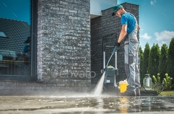 ucasian Men in His 30s Washing Concrete Bricks Driveway in Sunny Summer Day. Cleaning Around the House Concept.