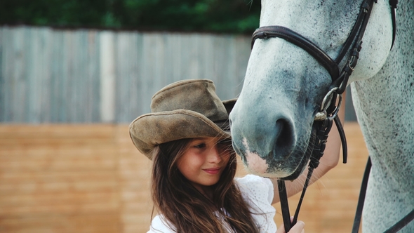 Young Happy Girl Caressing Her Pretty White Horse on the Area