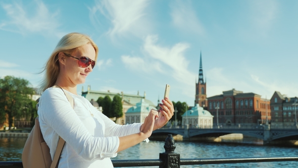 A Young Woman Photographes Herself with a Smartphone Against the Backdrop of Stockholm's City Line