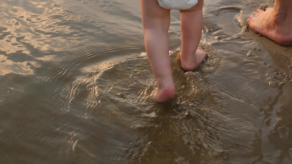 Child Walks on Water on Beach with Her Mother Splashing Water Around