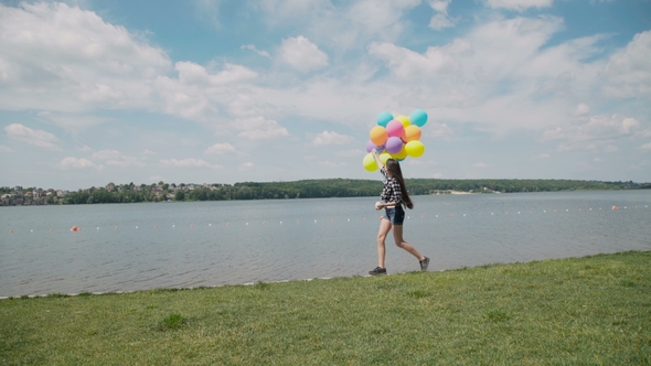 Pretty Girl Walks on the River Bay with Colourful Balloons and Looks on Water