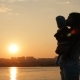 A Young Mother Kisses Her Little Son While Standing By the River at Sunset - VideoHive Item for Sale