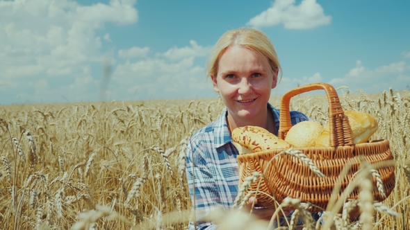 Woman Farmer with a Basket with Bread and Rolls on a Mature Wheat Field. Good Harvest, Organic