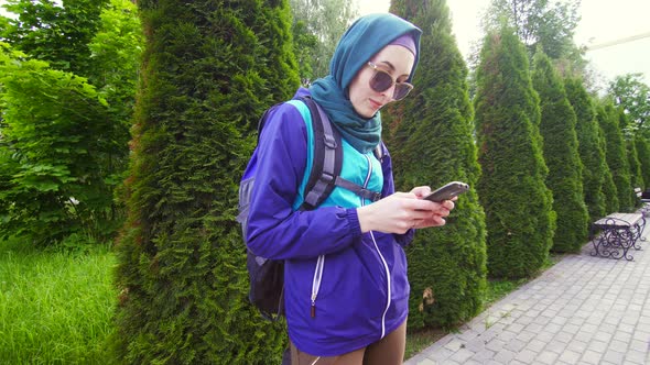 Girl Tourist in Hijab in a Backpack Uses the Phone