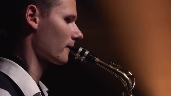 A Young Retro Stylish Guy Plays on the Golden Shiny Saxophone on Stage. Dark Studio with Smoke and