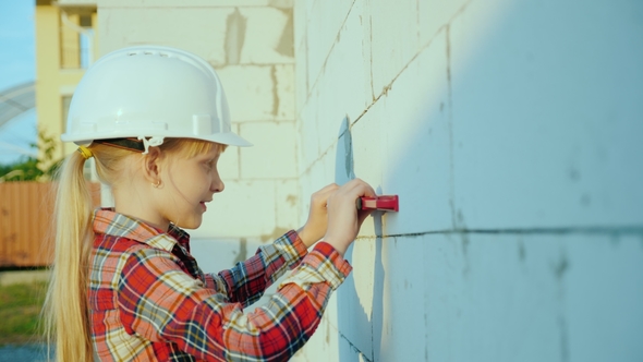 A Little Girl Builder in a White Helmet Checks the Level