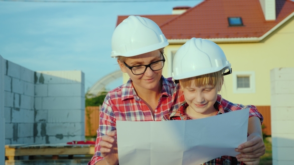 A Little Girl in a Helmet with a Young Mother Is Studying the Architectural Plan