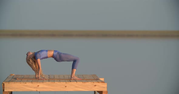 Fit Woman with Blonde Hair is Stretching on a Platform in the Lake Sports