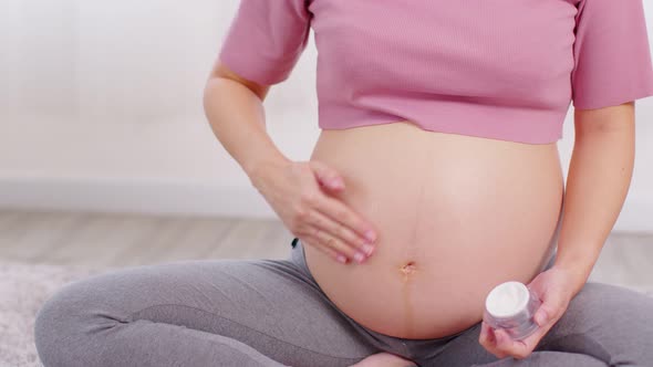 Close up Pregnant Woman sitting on bed holding and stroking apply cream