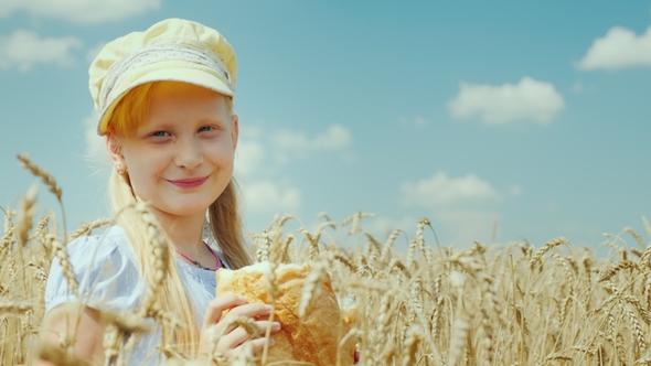 A Girl with a Loaf of Bread Stands on a Wheat Field, Looks at the Camera