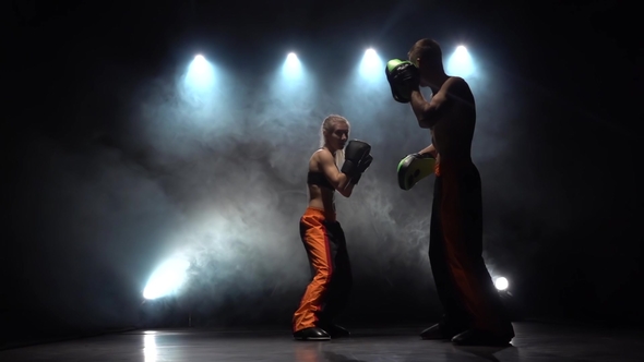 Guy with a Girl Boxing Gloves Beating in the Ring in the Dark, They Are Preparing for a Kickboxing