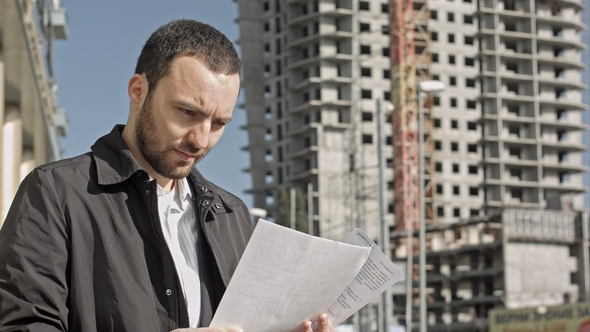 Man with Documentation Near Construction of a New Building
