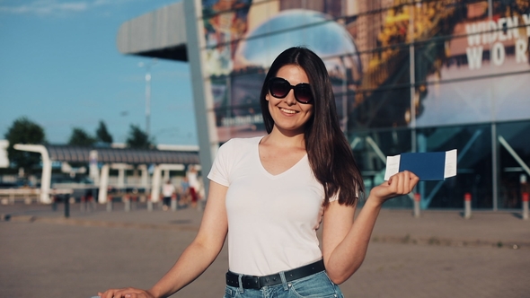 Portrait of Smiling Young Woman Holding Her Passport with Ticket in Hands Standing Near the Airport