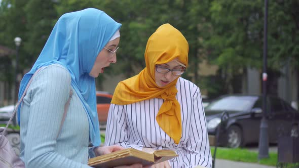 Two Muslim Women Students in Traditional Scarves with Books in Their Hands Communicate in the Park