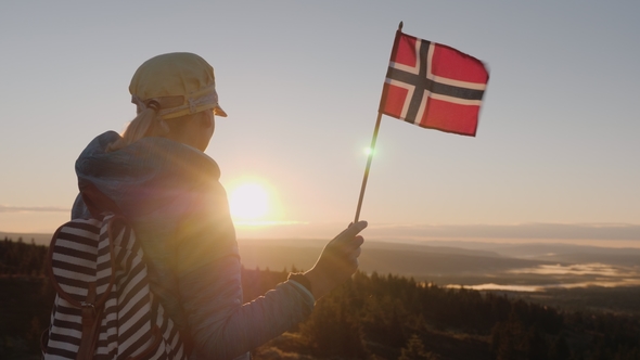 A Traveler with the Flag of Norway in His Hand Meets the Sunrise on the Top of the Mountain. Enjoys