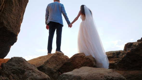 Unrecognizable Wedding Couple Holding Hands on Sunset or Sunrise Background. Bride and Groom