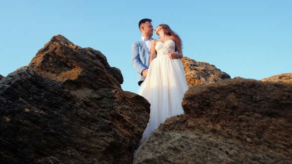 Beautiful Young Wedding Couple Standing on Sea Shore with Rocks. Newlyweds Spend Time Together