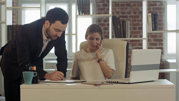 Portrait of a Woman Making a Phone Call While Her Colleague Is Working in a Office