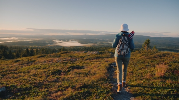An Active Woman with a Backpack and a Norwegian Flag Is Walking Along a Mountain Path. Ahead Is an