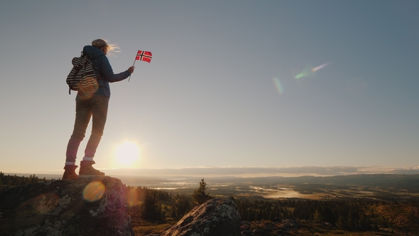 A Woman Stands on Top of a Mountain Holding the Flag of Norway in Her Hand