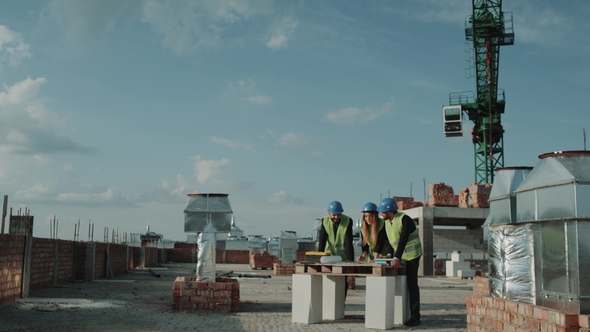 Young Engineers Have a Discussion About the Building Plan Map at Construction Site alt