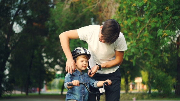 Caring Father Is Putting Safety Helmet on His Little Son's Head