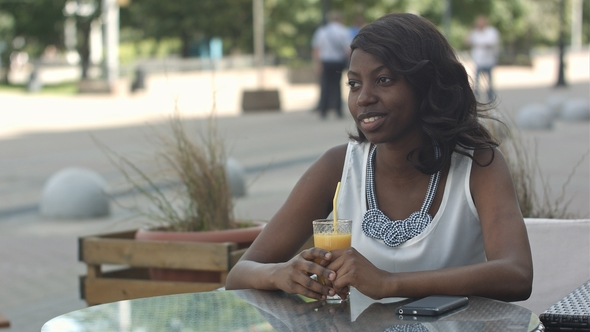 Portrait of Young African Woman Sipping Orange Juice and Dreaming While Sitting in Café
