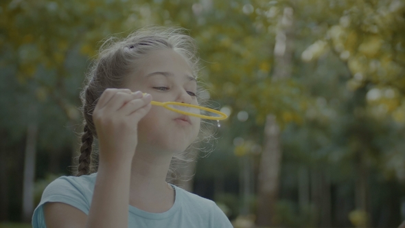 Cute Preteen Girl Blowing Soap Bubbles in Park