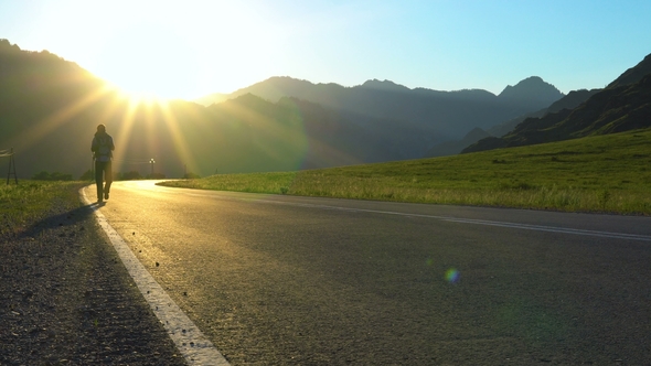 A Young Tourist with a Backpack Goes on the Road in a Mountainous Area