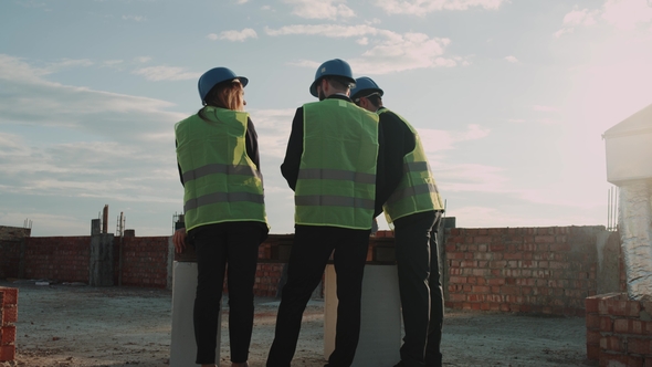 Workteam Engineers Analyzing the Scheme Map of Building on Construction Site, Wearing a Safety alt