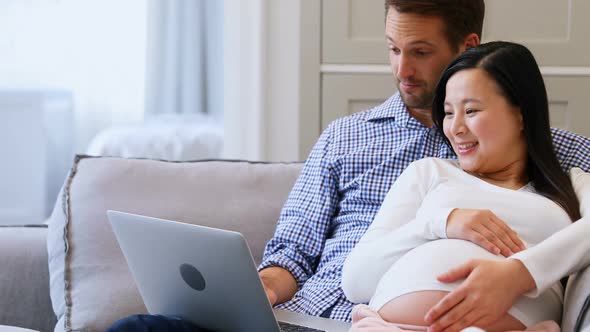 Pregnant couple using laptop on bed in living room